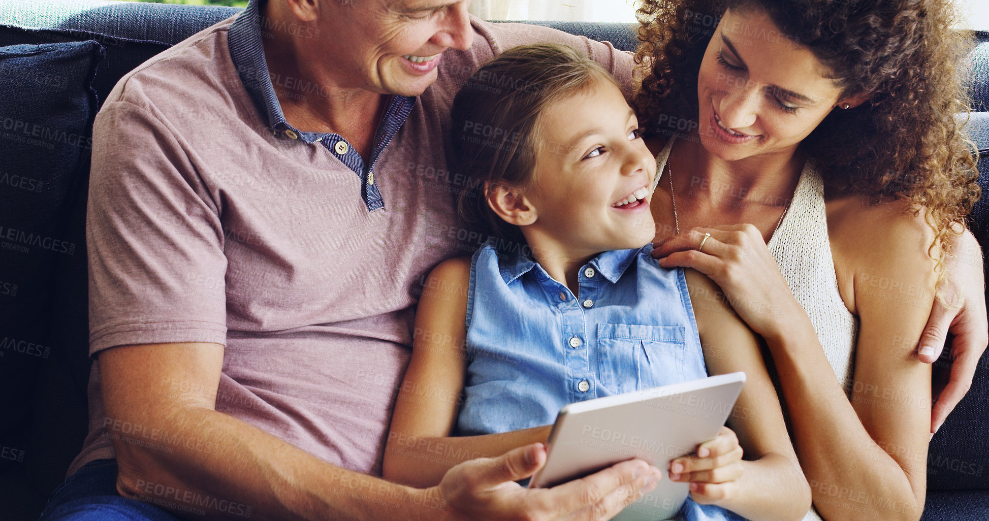 Buy stock photo Shot of a cute little girl using a digital tablet with her mother and father on the sofa at home