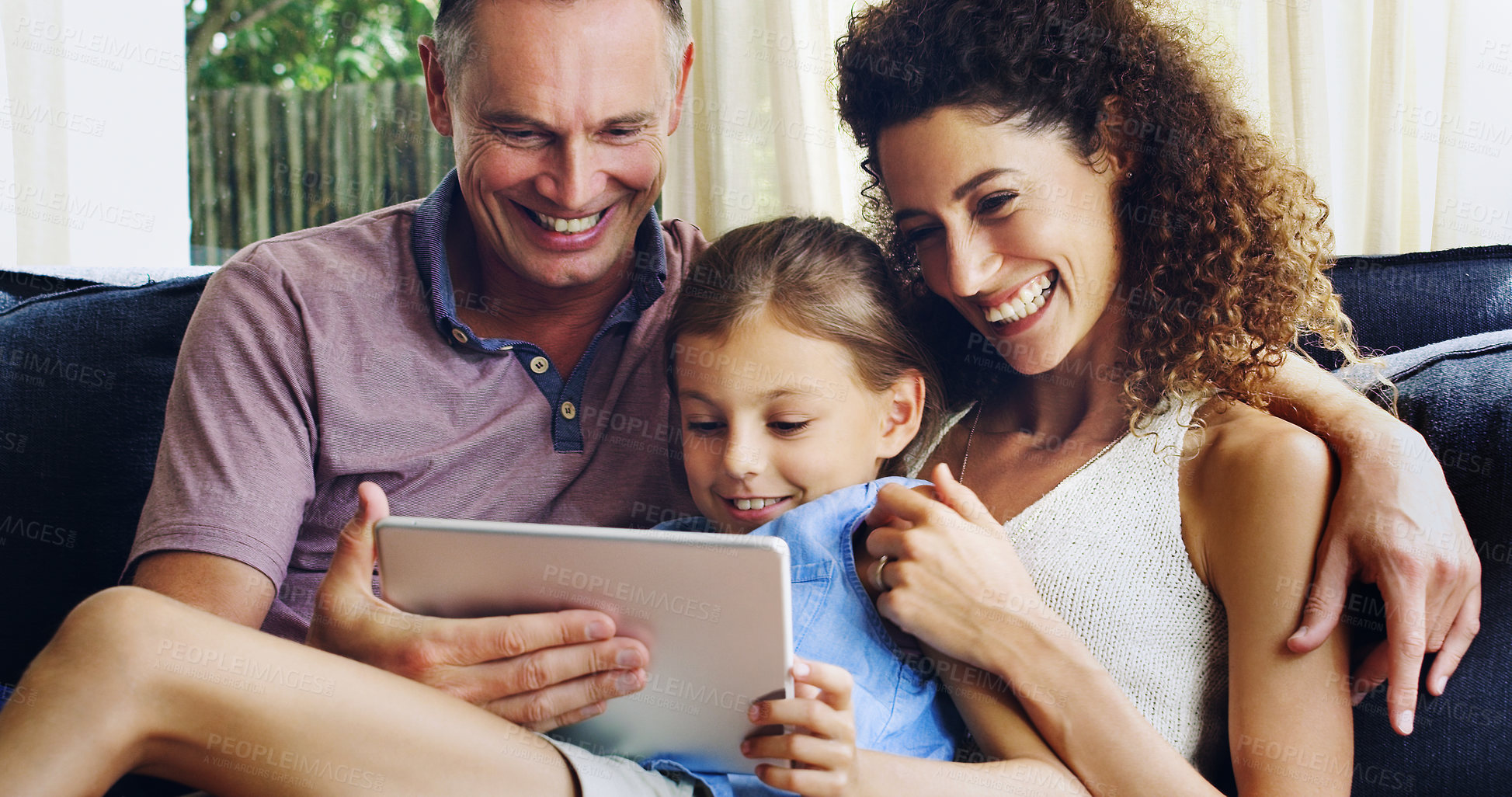 Buy stock photo Shot of a cute little girl using a digital tablet with her mother and father on the sofa at home