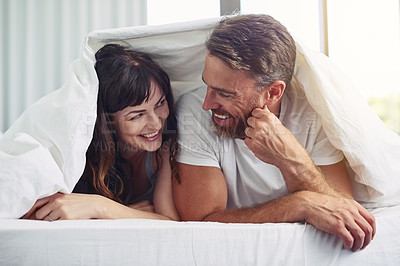 Buy stock photo Shot of a cheerful young couple crawling out of bed while having a laugh together during morning hours