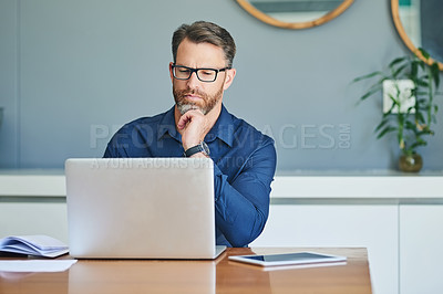 Buy stock photo Shot of a focussed middle aged man working on his laptop while contemplating at home during the day