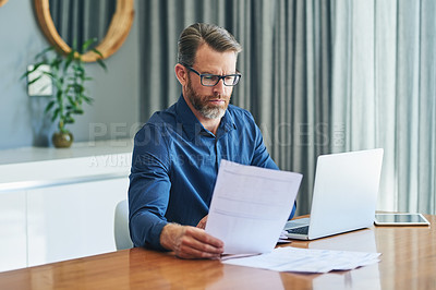 Buy stock photo Shot of a focussed middle aged businessman sorting out documents and working from home during the day