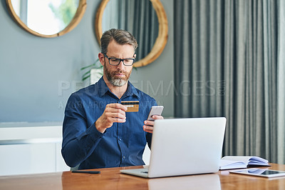 Buy stock photo Shot of a focussed middle aged businessman working on his laptop and paying bills with his credit card at home during the day
