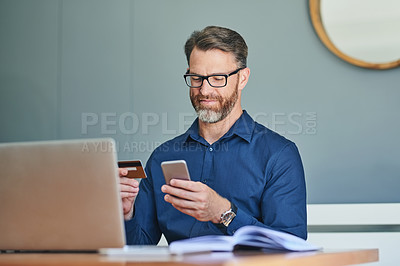 Buy stock photo Shot of a cheerful middle aged businessman working on his laptop and paying bills with his credit card at home during the day