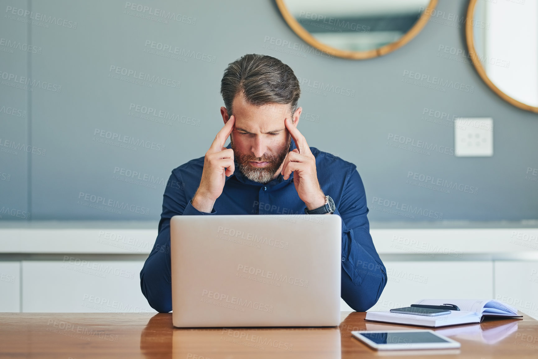 Buy stock photo Shot of a stressed out middle aged businessman working on his laptop while trying to think at home during the day