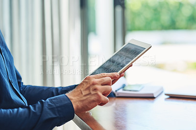Buy stock photo Shot of an unrecognizable person browsing on a digital tablet while being seated at a table at home