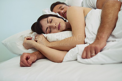 Buy stock photo Shot of a relaxed young couple sleeping in each other's arms in bed during morning hours