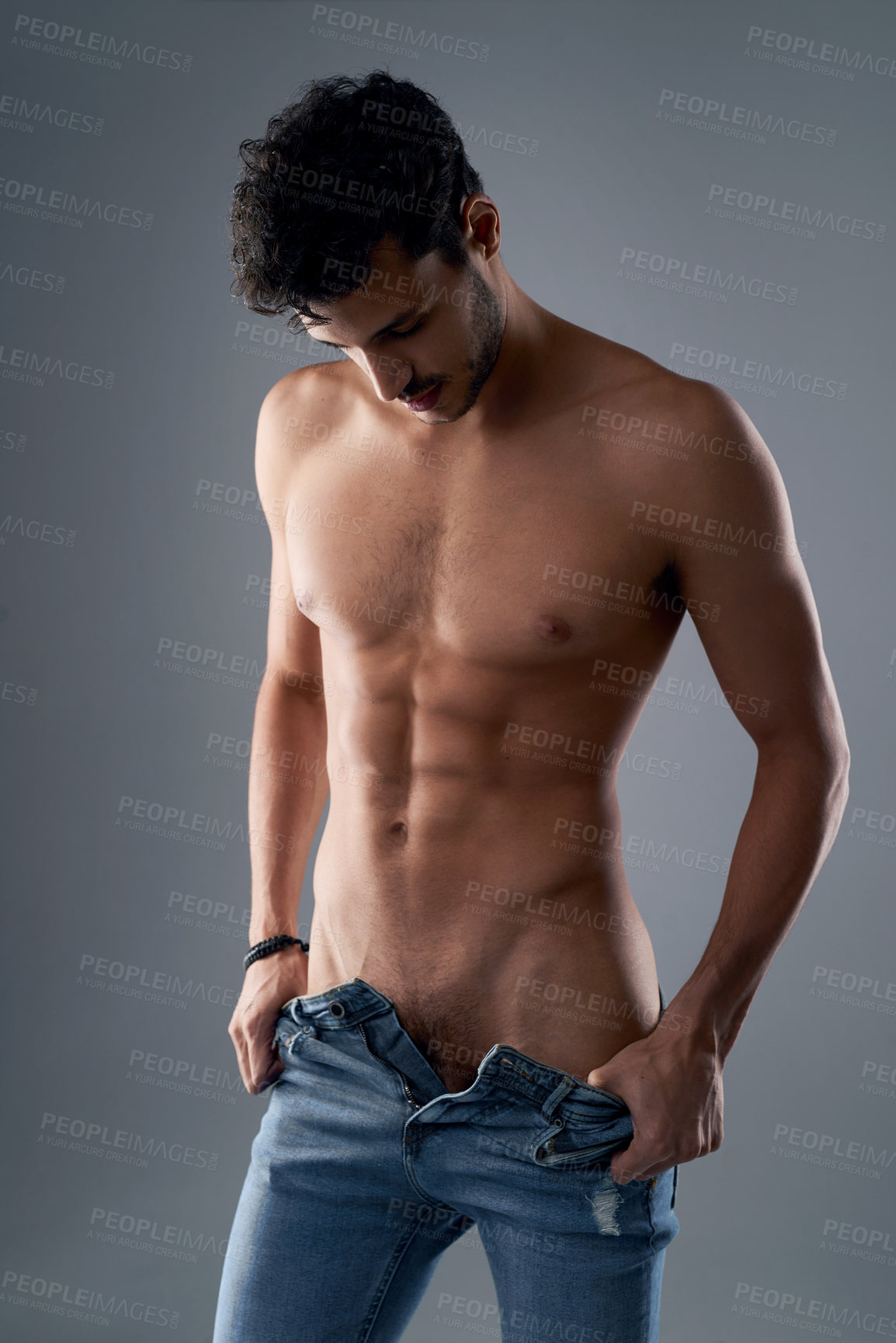 Buy stock photo Studio shot of a handsome young shirtless man undressing against a grey background
