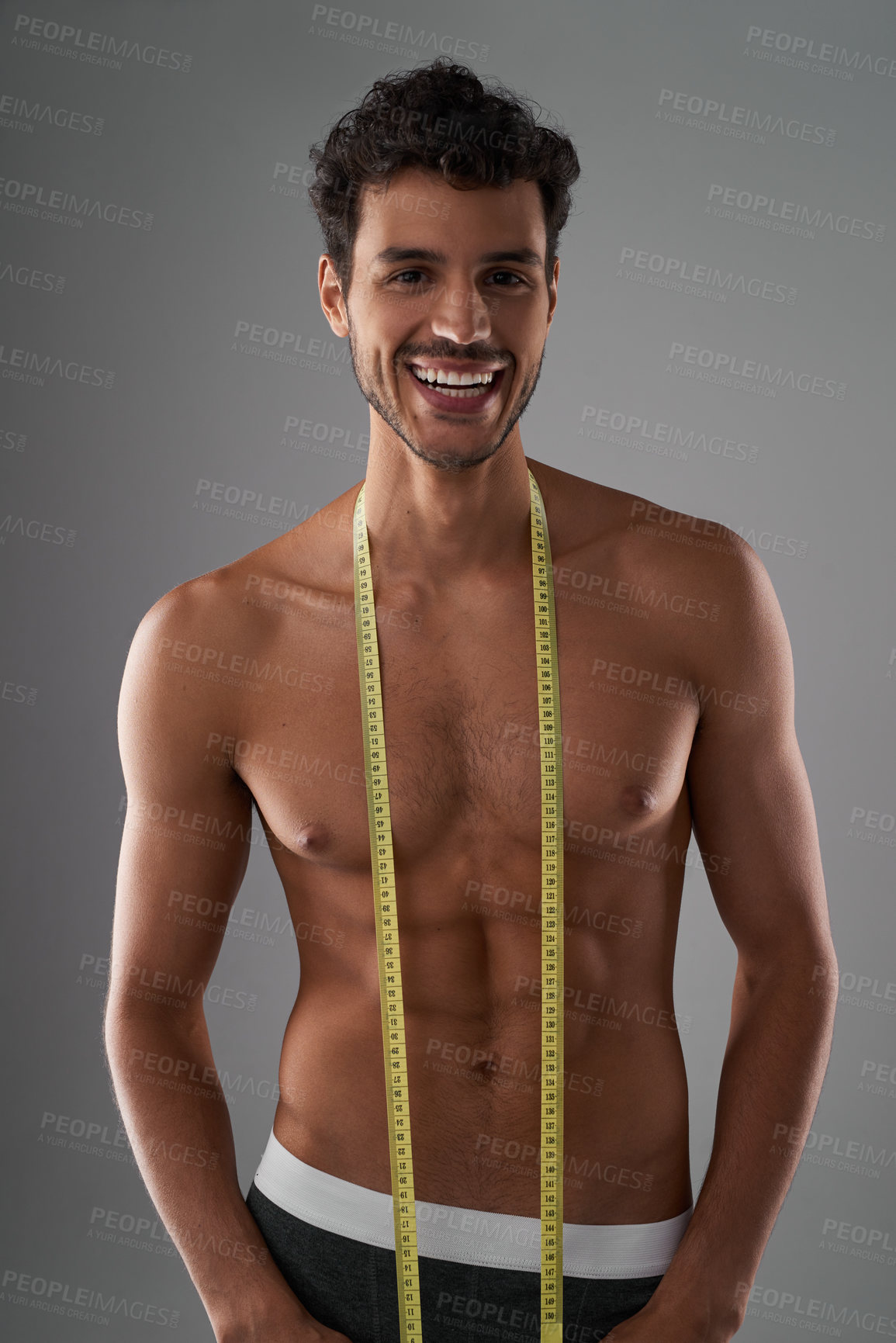 Buy stock photo Studio shot of a handsome young shirtless man posing with a measuring tape against a grey background