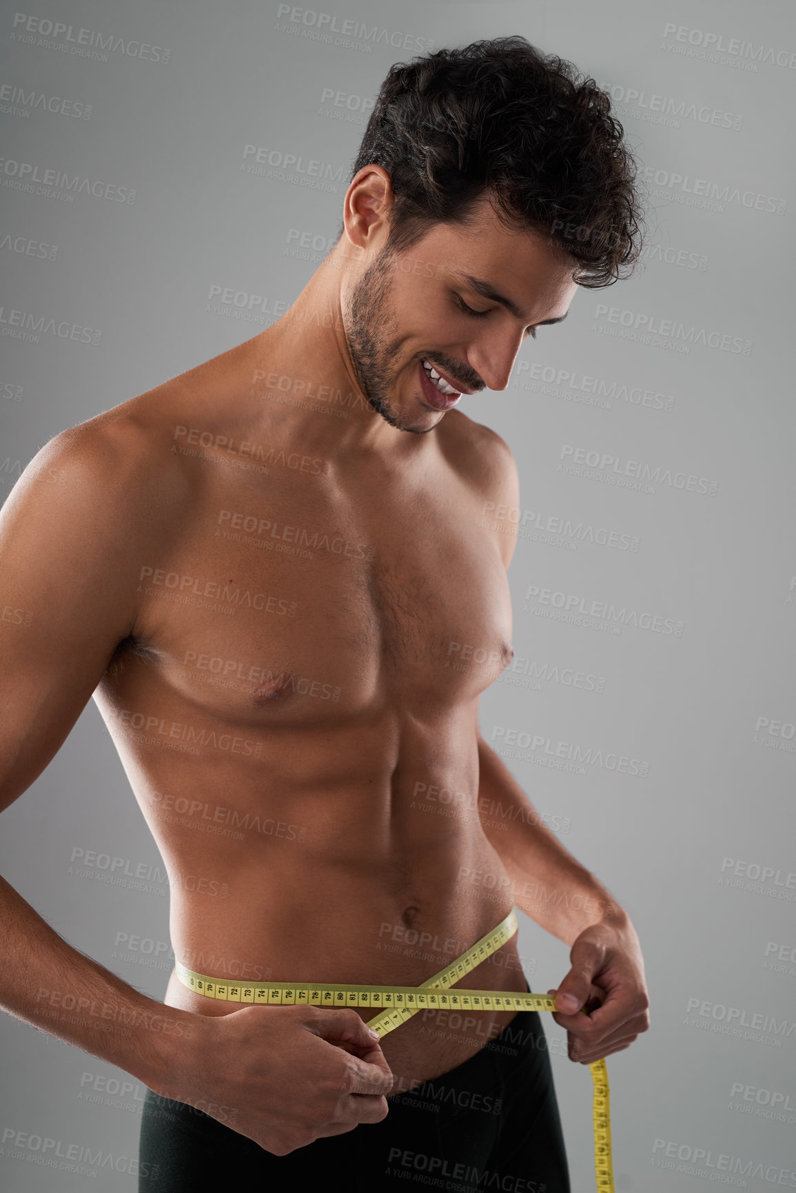 Buy stock photo Studio shot of a handsome young shirtless man measuring his midsection against a grey background
