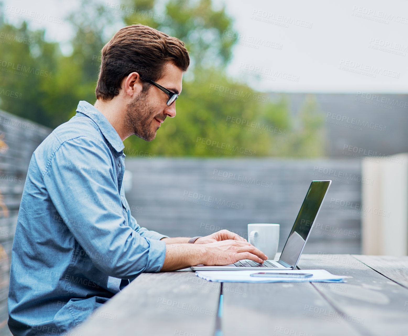 Buy stock photo Shot of a handsome young man using a laptop outdoors