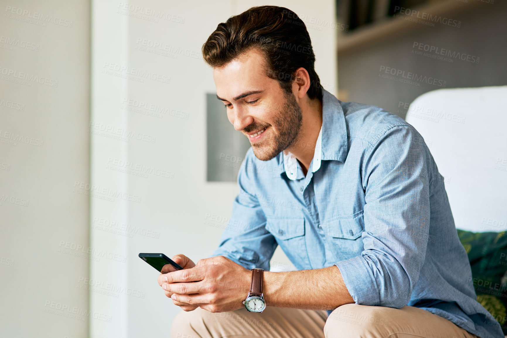 Buy stock photo Shot of a handsome young man texting on a cellphone at home