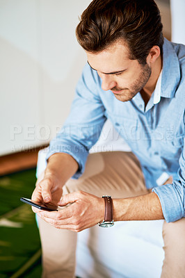 Buy stock photo Shot of a handsome young man texting on a cellphone at home