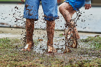 Buy stock photo Low angle shot of two unrecognizable children jumping around in mud outside during a rainy day