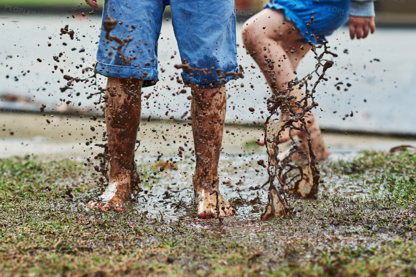 Buy stock photo Low angle shot of two unrecognizable children jumping around in mud outside during a rainy day