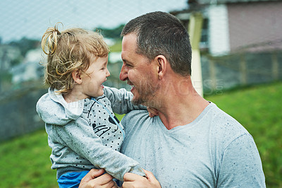 Buy stock photo Shot of a cheerful little girl being held by her father while they look at each other's eyes outside during a rainy day