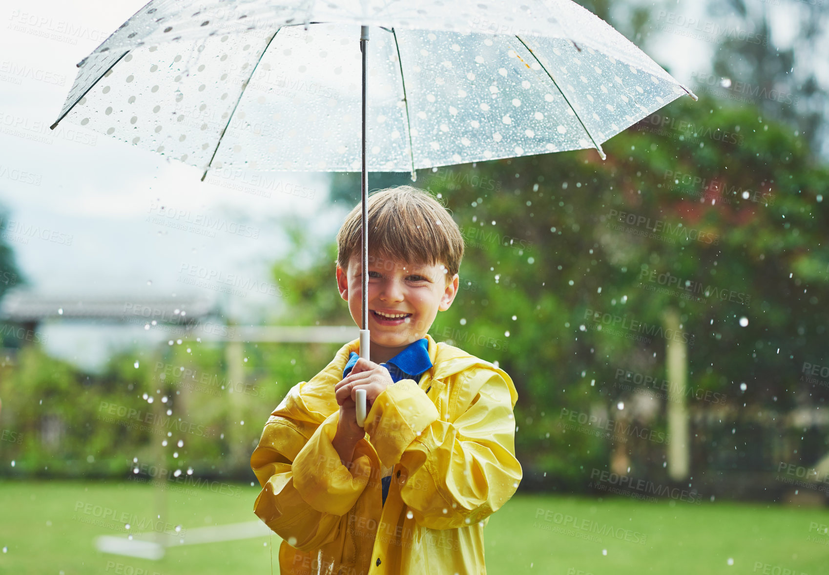 Buy stock photo Portrait of a cheerful little boy standing with an umbrella outside on a rainy day
