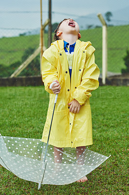 Buy stock photo Shot of a cheerful little boy standing with an umbrella while opening his mouth to catch rain drops outside on a rainy day