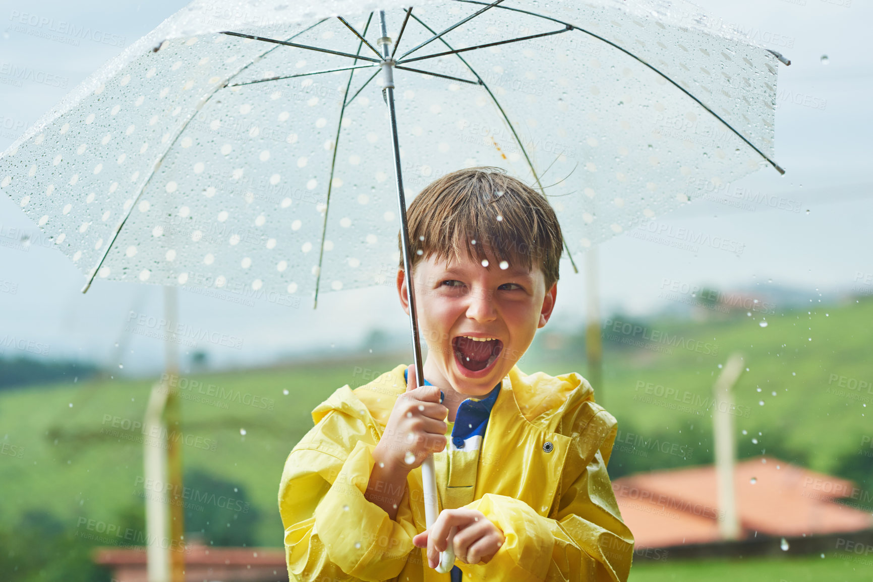 Buy stock photo Portrait of a cheerful little boy standing with an umbrella outside on a rainy day