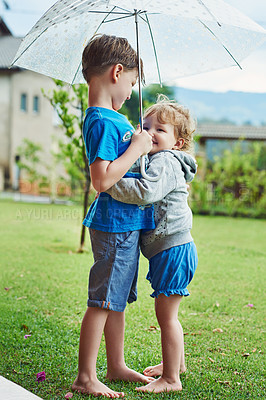 Buy stock photo Shot of a cheerful little boy and girl standing together under an umbrella outside during a rainy day