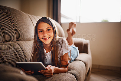Buy stock photo Full length portrait of a young girl using her tablet while lying on a sofa at home