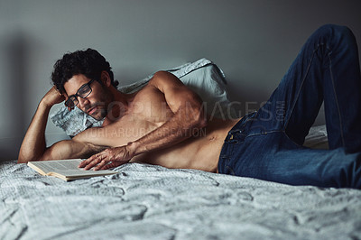 Buy stock photo Cropped shot of a handsome young shirtless man reading a book on his bed at home