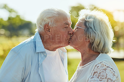 Buy stock photo Shot of a happy senior couple sharing a loving kiss in the park