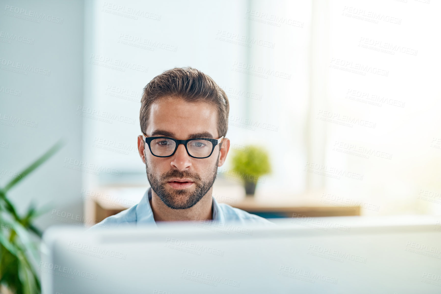 Buy stock photo Shot of a young businessman working on a computer in an office