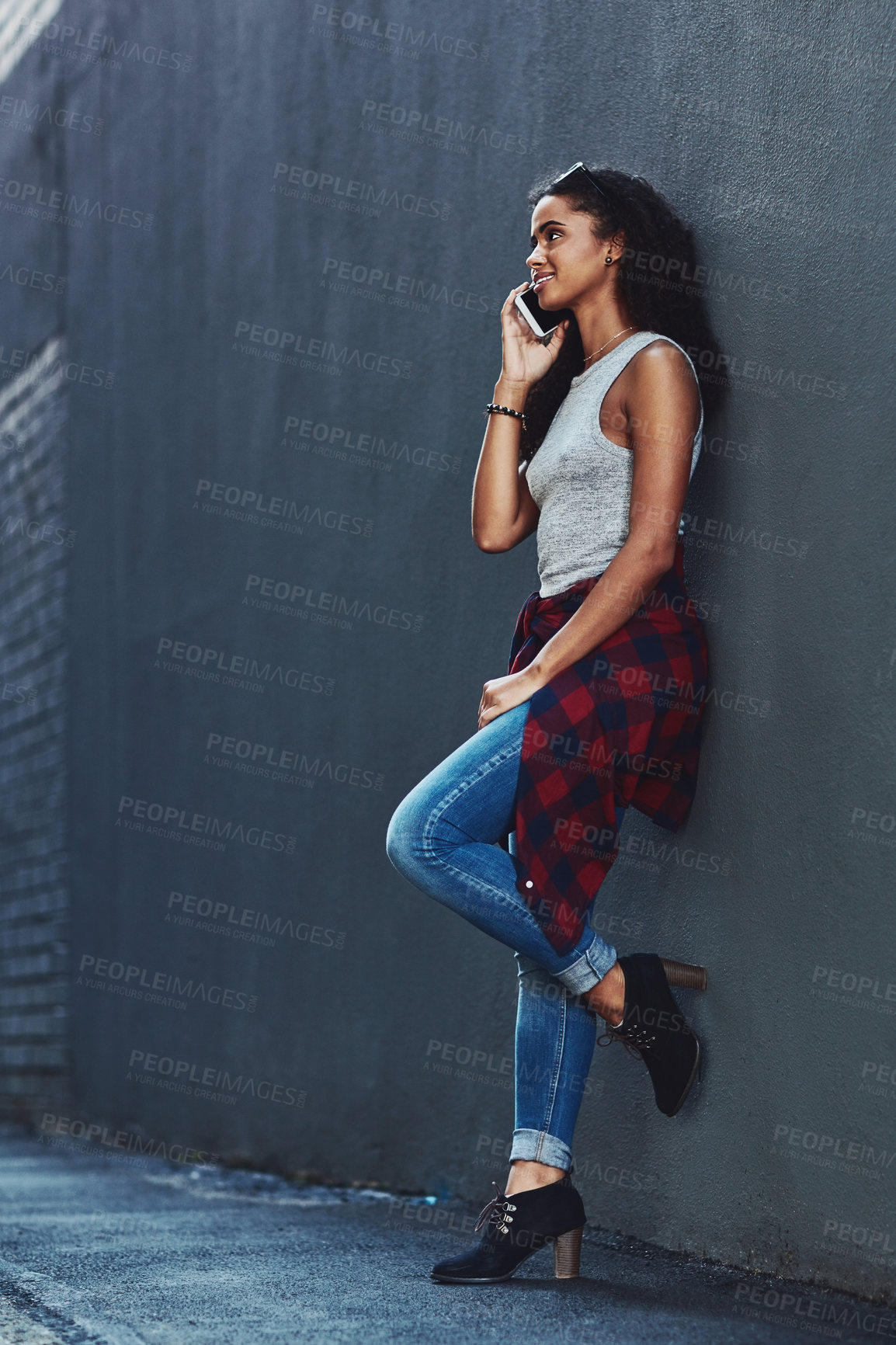 Buy stock photo Shot of an attractive young woman on a call posing against a wall in the city