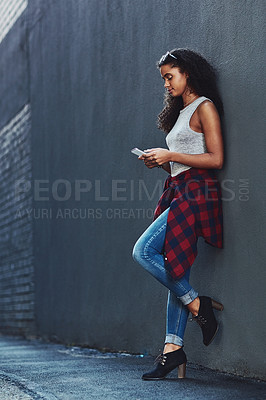 Buy stock photo Shot of an attractive young woman using a cellphone posing against a wall in the city