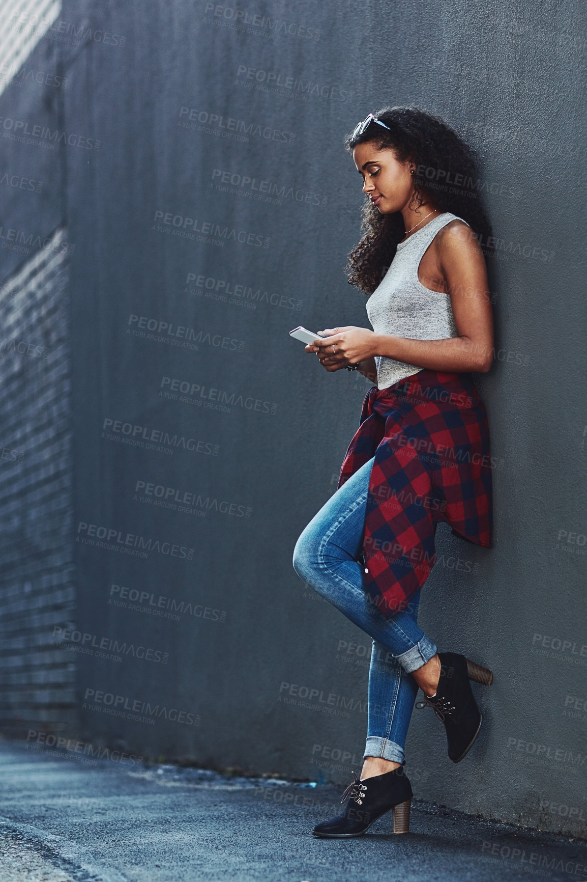 Buy stock photo Shot of an attractive young woman using a cellphone posing against a wall in the city
