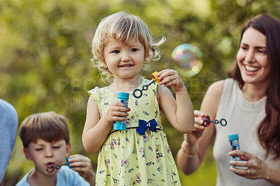Buy stock photo Shot of an adorable little girl blowing bubbles with her family outdoors