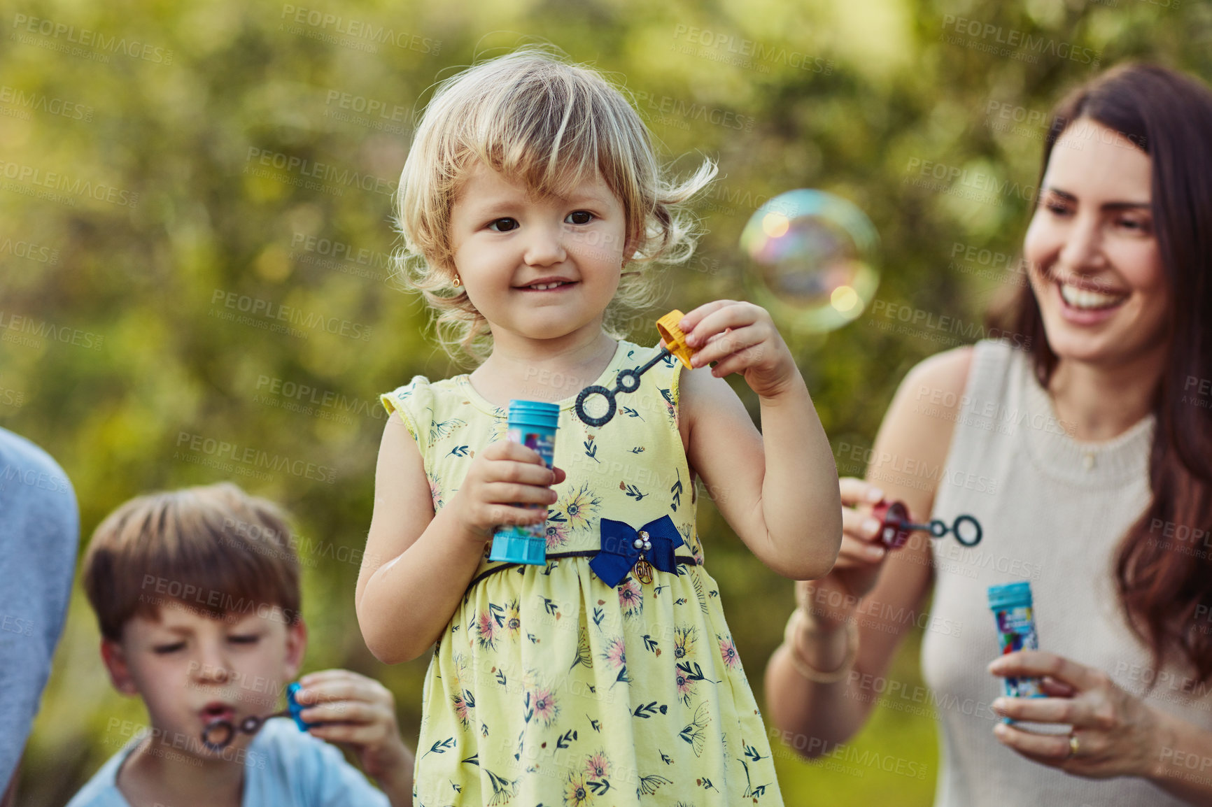 Buy stock photo Shot of an adorable little girl blowing bubbles with her family outdoors
