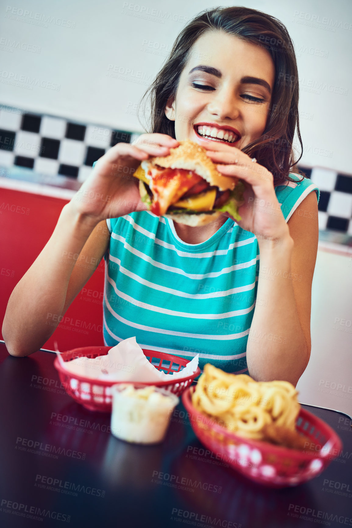Buy stock photo Cropped shot of an attractive young woman enjoying a burger in a retro diner
