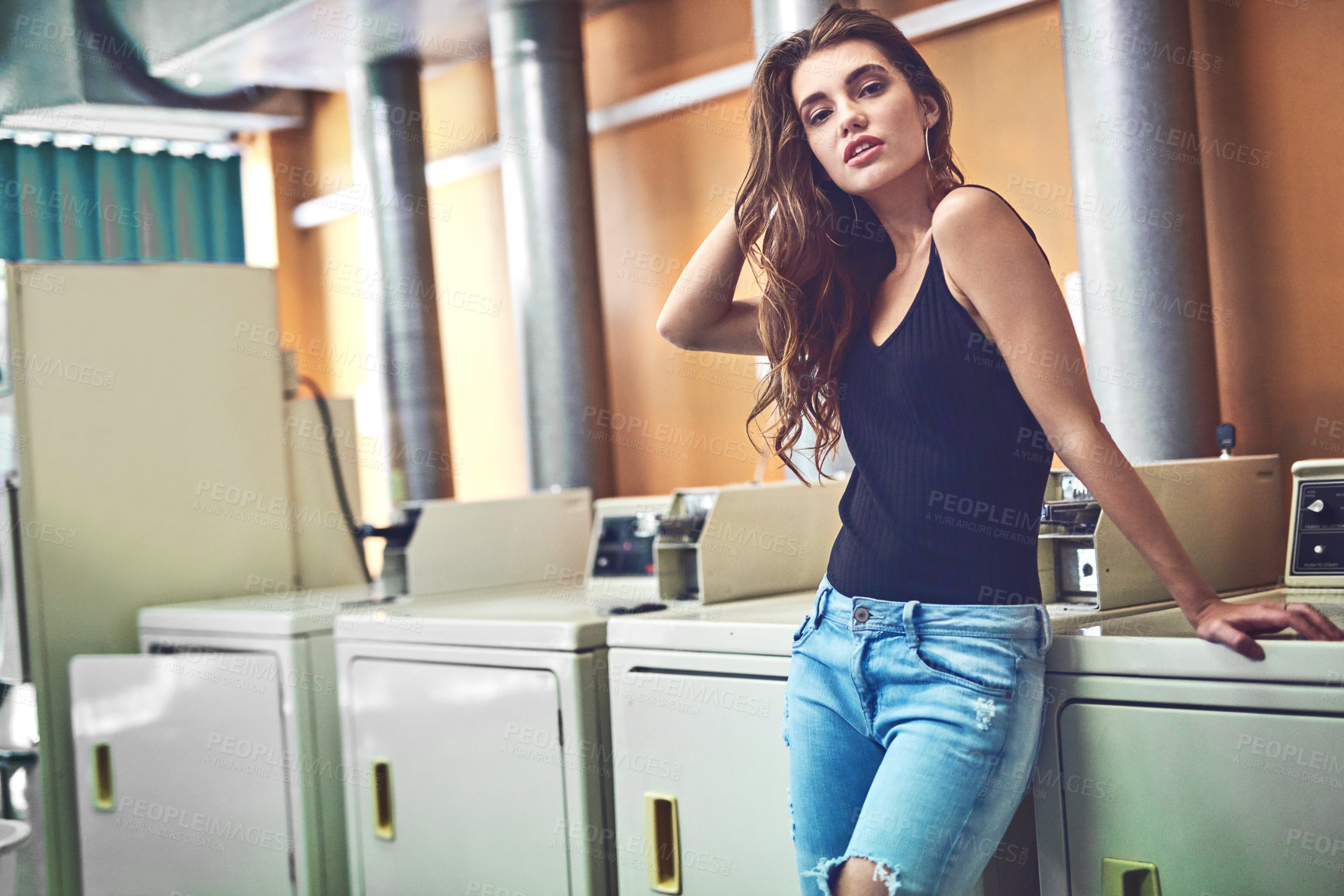 Buy stock photo Portrait of an attractive young woman standing in a laundry room while waiting for washing to be done during the day