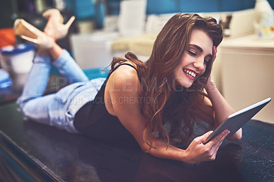 Buy stock photo Shot of an attractive young woman lying on top of a counter while browsing on a digital tablet to pass time in a laundry room
