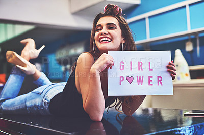 Buy stock photo Shot of an attractive young woman lying on top of a counter while holding a sign saying 