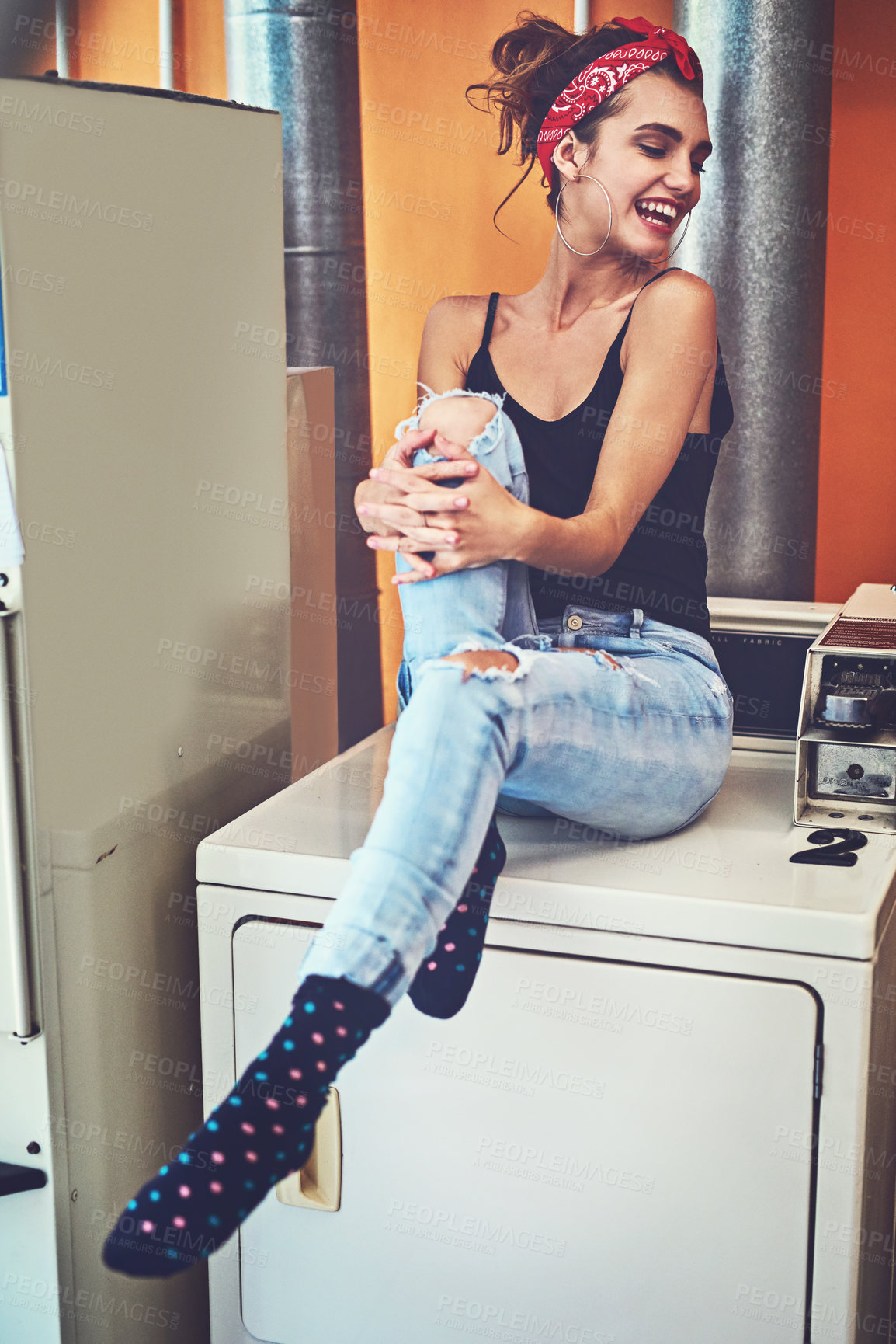 Buy stock photo Shot of an attractive young woman seated on a washing machine while waiting for the washing to be washed inside of a laundry room