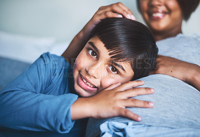 Buy stock photo Cropped portrait of an adorable little boy lying on his mother's lap while trying to hear the baby