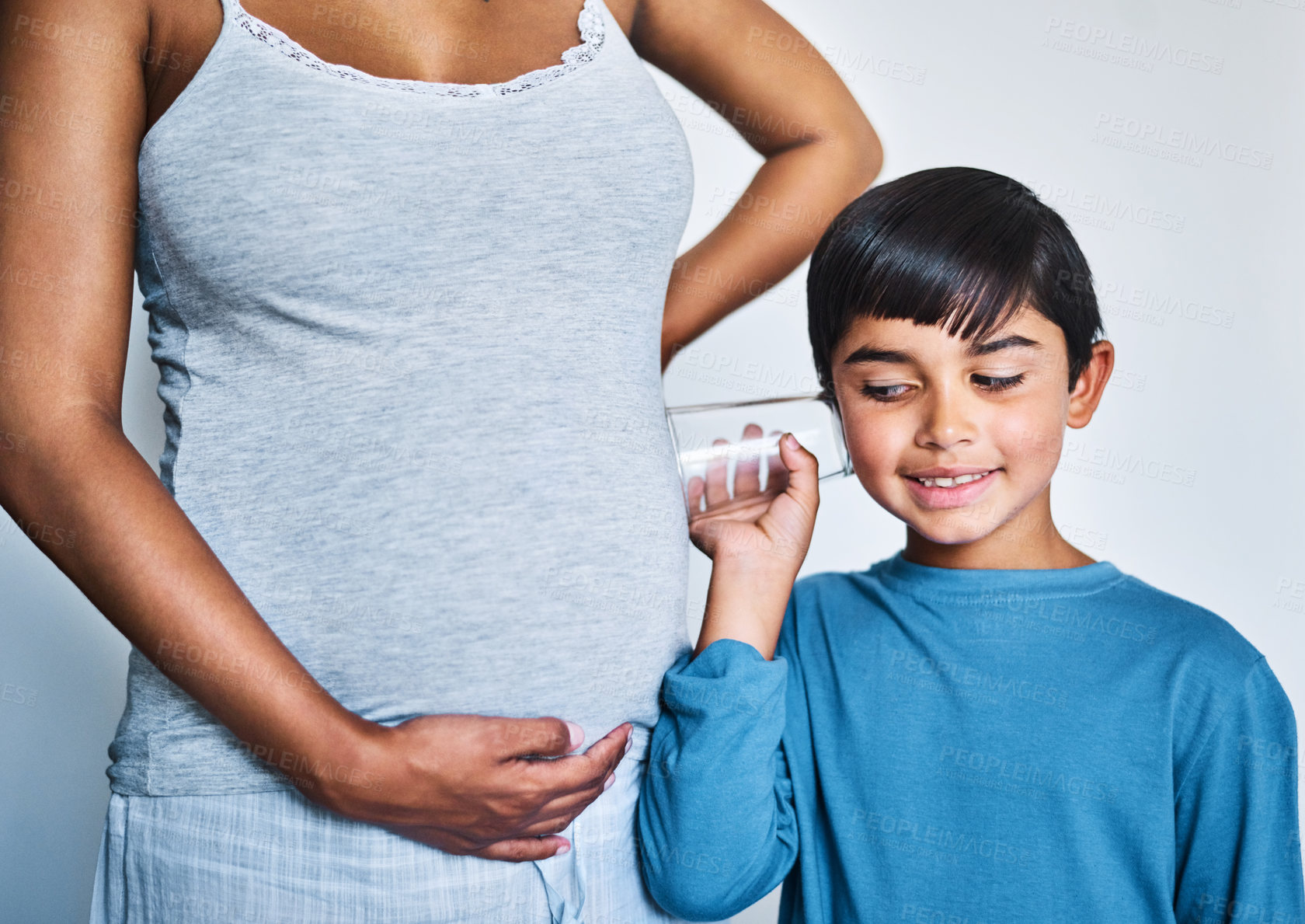Buy stock photo Cropped shot of an adorable little boy using a glass to listen to the baby inside his mother's stomach