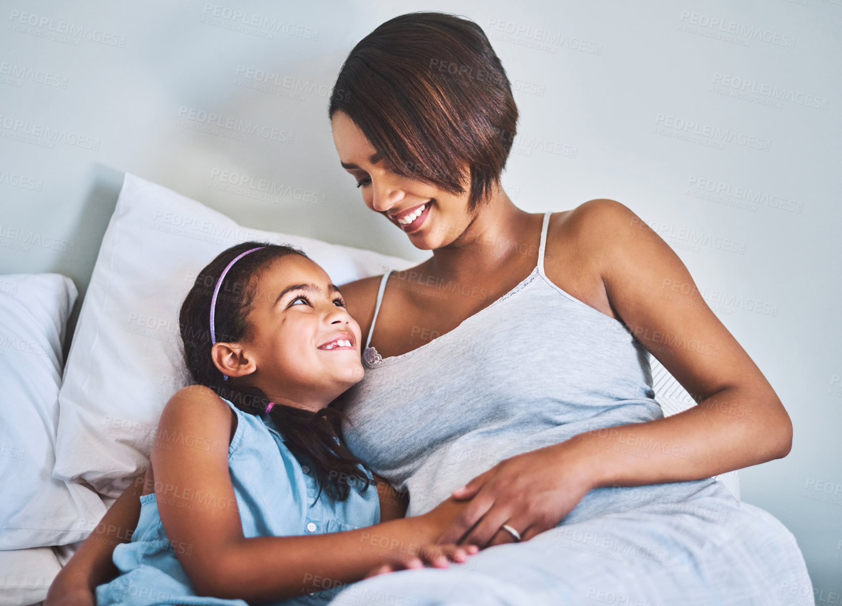 Buy stock photo Shot of a cheerful little girl relaxing on the bed with her pregnant mother at home during the day