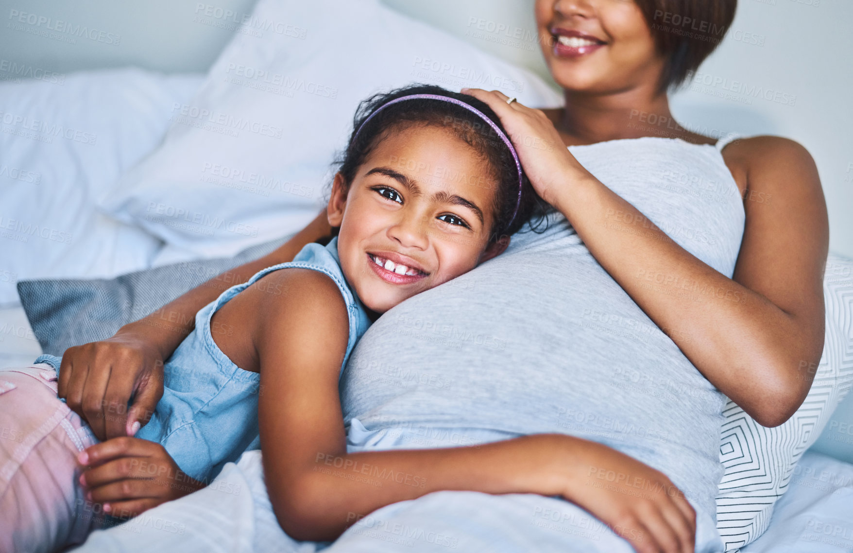 Buy stock photo Portrait of a cheerful little girl relaxing on the bed with her pregnant mother at home during the day
