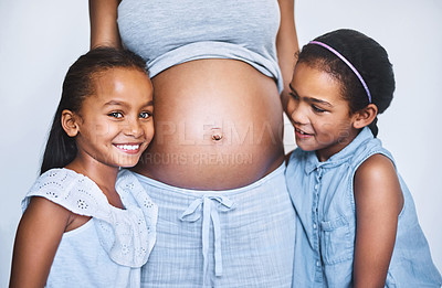 Buy stock photo Portrait of two cheerful little girls standing next to their pregnant mother at home during the day