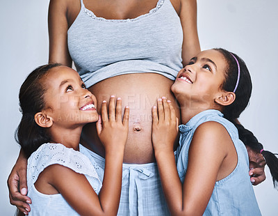 Buy stock photo Shot of two cheerful little girls standing next to their pregnant mother at home during the day