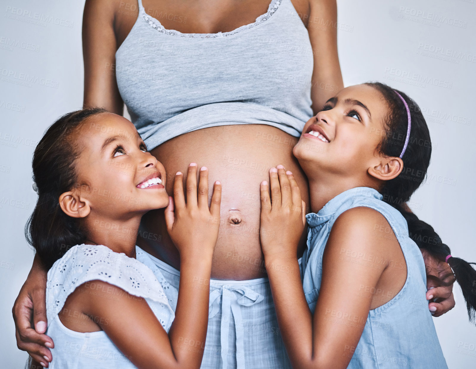 Buy stock photo Shot of two cheerful little girls standing next to their pregnant mother at home during the day