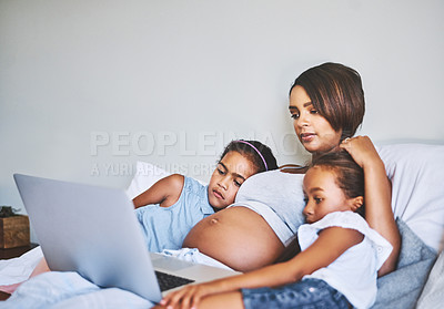 Buy stock photo Shot of two focused little girls relaxing next to their pregnant mother while watching a movie on a laptop at home during the day