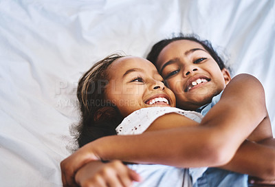 Buy stock photo Portrait of two cheerful little girls  with arms around each other while lying on a bed at home during the day