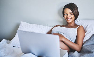 Buy stock photo Portrait of a cheerful pregnant woman lying on a bed at home relaxing while browsing on a laptop during the day