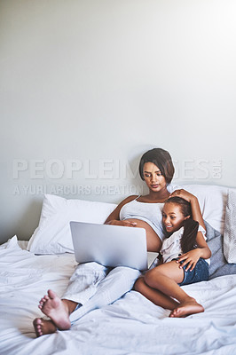Buy stock photo Shot of a cheerful little girl and her mother lying on a bed while watching a movie on a laptop at home