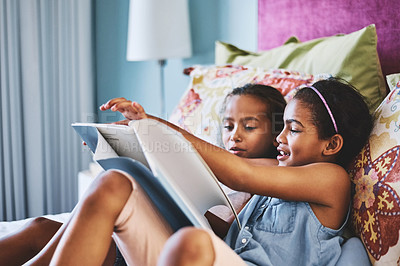 Buy stock photo Shot of two cheerful little girls reading a storybook together at home during the day