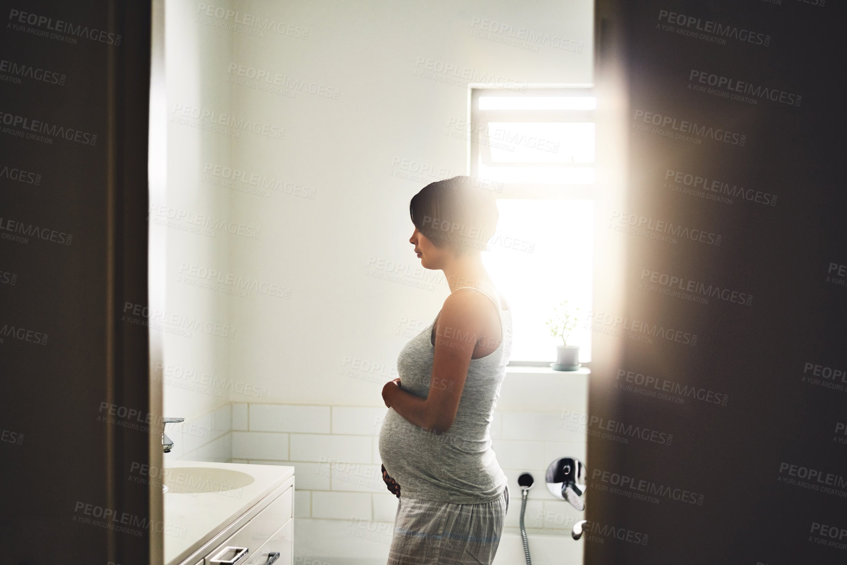 Buy stock photo Shot of a pregnant young woman standing in the bathroom at home